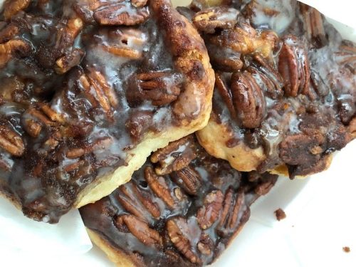 Two pecan sticky buns drizzled with a glossy caramel glaze, resting in a white container.