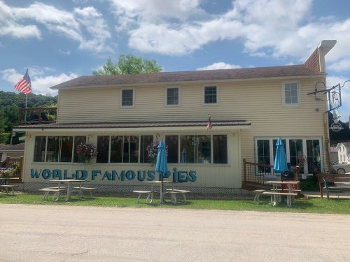 A two-story building with "World Famous Pies" sign, outdoor seating, and American flags, set against a blue sky.