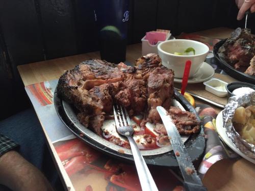 A plate of grilled meat with cut pieces, forks, and a side of sauce, set on a wooden table.