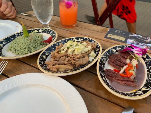 Three plates of food: green rice, shredded meat with cabbage, and sliced beef garnished with flowers, on a wooden table.