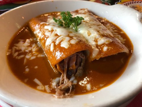 Two enchiladas topped with melted cheese, served in a rich red sauce, garnished with a sprig of parsley.