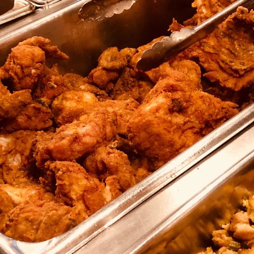 A close-up of crispy, golden-brown fried chicken pieces in a serving tray with tongs.