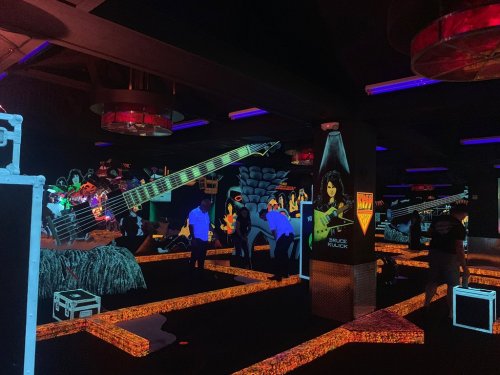 A vibrant, neon-lit indoor space featuring oversized guitars and colorful murals, with people exploring the area.