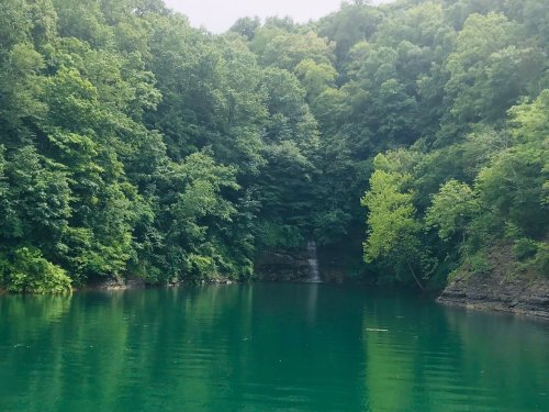 A serene lake surrounded by lush green trees and a small waterfall in the background.