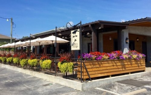 A charming restaurant exterior with colorful flowers, patio umbrellas, and a welcoming atmosphere on a sunny day.