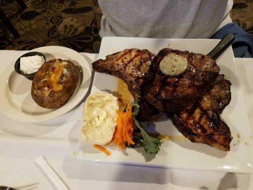 A plate with grilled steak, a baked potato with cheese, and a biscuit, garnished with carrots and greens.