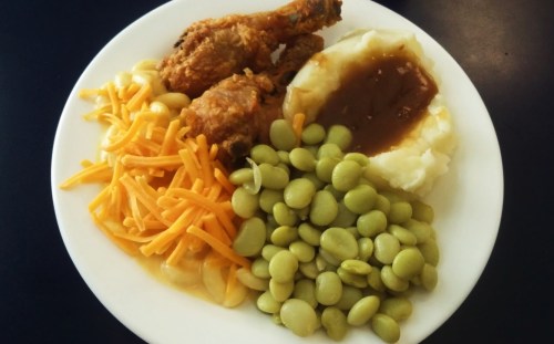 A plate of fried chicken, mashed potatoes with gravy, green lima beans, and shredded cheese.