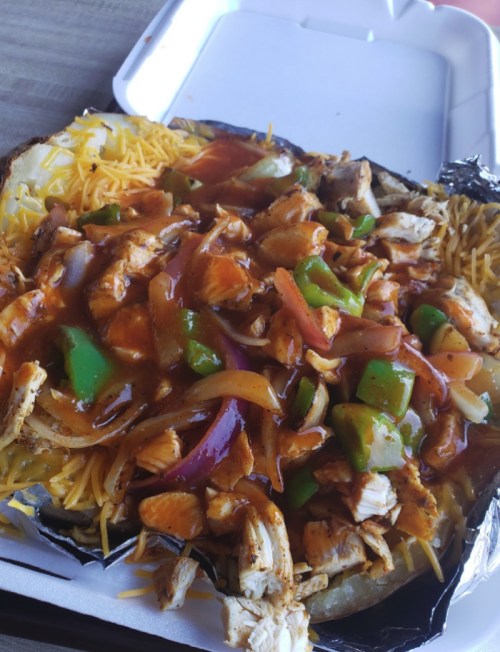 A loaded nacho dish with shredded chicken, cheese, and colorful peppers topped with a savory sauce.