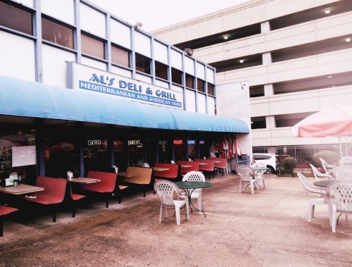 Exterior of Al's Deli & Grill with outdoor seating and a blue awning, next to a parking garage.