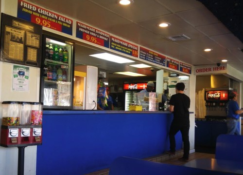 A casual restaurant counter with menu boards, drinks, and a customer ordering at the register.