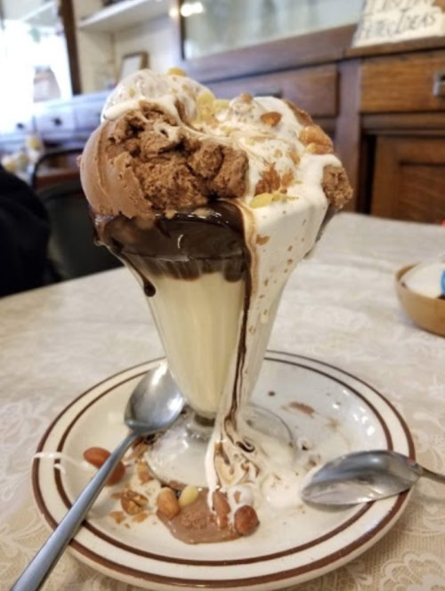 A tall ice cream sundae overflowing with chocolate and vanilla ice cream, topped with whipped cream and nuts.