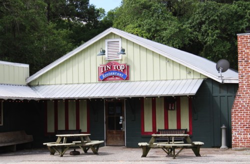 Exterior of Tin Top Restaurant, featuring a green and white building with picnic tables outside and a sign above the door.