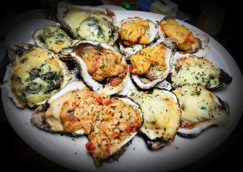 A platter of baked oysters topped with various fillings, garnished with herbs.
