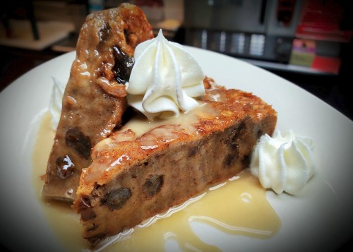 A slice of bread pudding topped with whipped cream and drizzled with a sweet sauce on a white plate.
