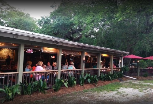 A cozy outdoor dining area with people enjoying meals, surrounded by greenery and string lights in the evening.
