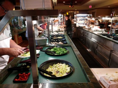 A buffet with various salad ingredients and dishes being prepared by staff in a restaurant setting.