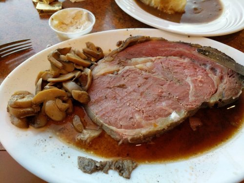 A plate of medium-rare prime rib with mushrooms and gravy on the side.