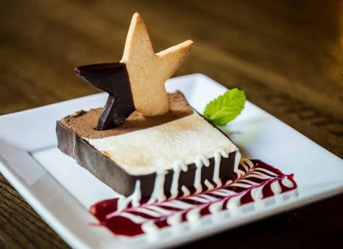 A dessert featuring layered chocolate and vanilla ice cream, topped with a star-shaped cookie and raspberry sauce.