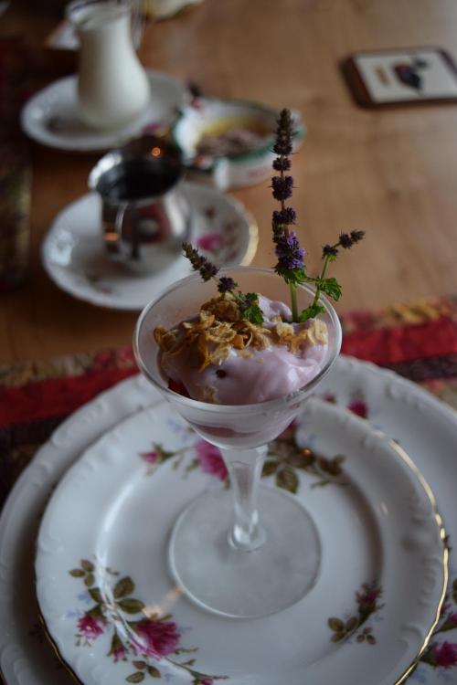 A dessert in a glass topped with yogurt, granola, and lavender, served on a floral-patterned plate.