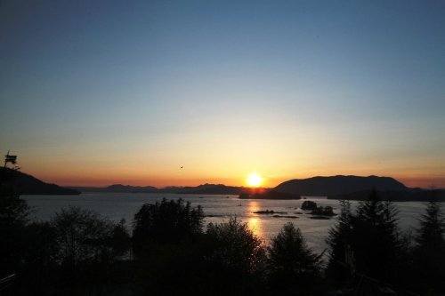 A serene sunset over a calm lake, with silhouettes of mountains and trees in the foreground.