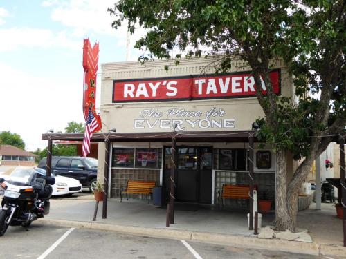 Exterior of Ray's Tavern, featuring a sign that reads "The Place for Everyone," with benches and a motorcycle parked outside.