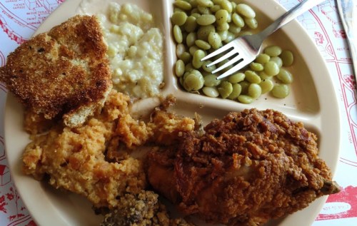 A plate of Southern comfort food featuring fried chicken, cornbread, collard greens, and creamy grits.