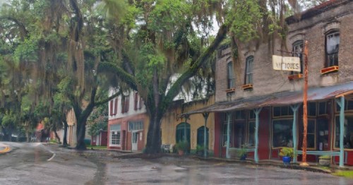 A quaint, historic street lined with trees draped in Spanish moss and charming old buildings.