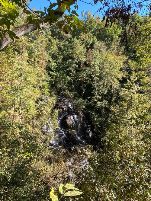 A serene waterfall cascades through lush green trees under a clear blue sky.