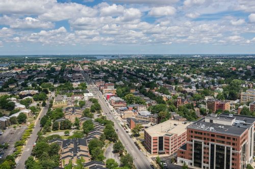 Aerial view of a cityscape featuring residential areas, roads, and a mix of buildings under a partly cloudy sky.