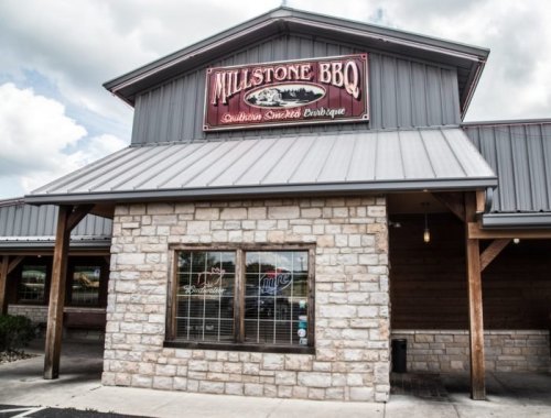 Exterior of Millstone BBQ restaurant featuring a stone facade and a large sign, with cloudy skies above.