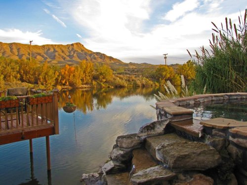 Scenic view of a calm river with mountains in the background, surrounded by trees and a wooden deck.