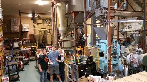 A group of three people stands in a large industrial facility filled with machinery and equipment for processing.