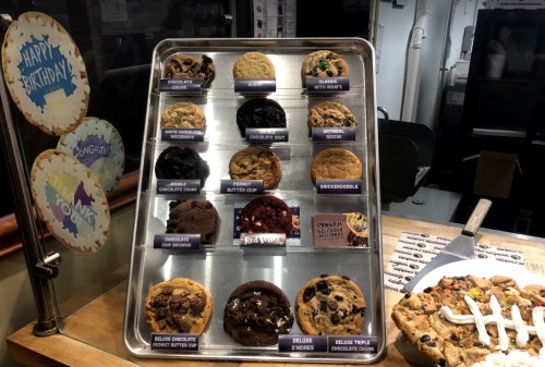 A tray of assorted cookies, including chocolate chip, peanut butter, and snickerdoodle, displayed in a bakery.