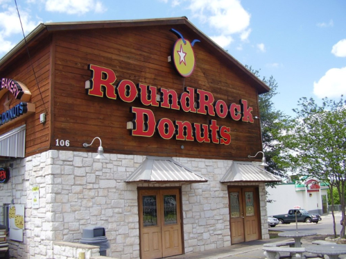 Signage of Round Rock Donuts on a wooden building, featuring a bright logo and stone facade.