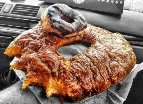 A large, flaky croissant donut with a chocolate-glazed donut on top, resting on a car dashboard.