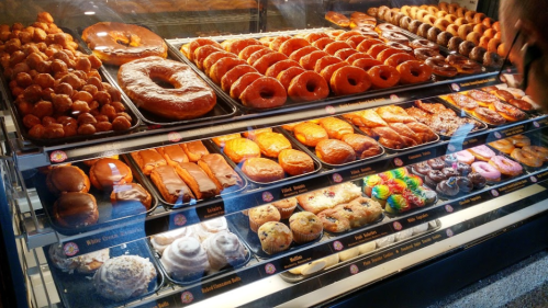 A display case filled with a variety of colorful donuts and pastries, including glazed, frosted, and sprinkled options.