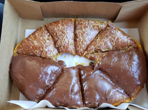 A round pastry with a golden-brown crust and a glossy chocolate glaze, cut into triangular pieces in a box.