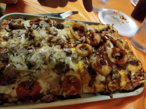 A large pizza divided into two halves: one with meat and onions, the other with barbecue sauce and onion rings.