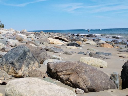 A rocky beach with smooth stones, gentle waves, and a clear blue sky in the background.