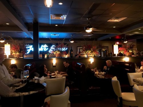 A dimly lit restaurant interior with booths, decorative plants, and a neon sign, featuring diners enjoying their meals.