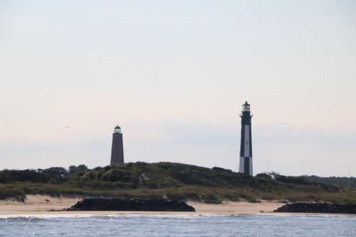 Two lighthouses stand on a grassy shore, with a calm sea in the foreground and a clear sky above.