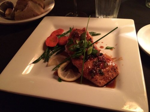 A plate of salmon fillet garnished with green onions, served with carrots, green beans, and lemon slices.