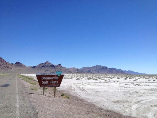 A road sign for Bonneville Salt Flats beside a wide, barren landscape with mountains in the background under a clear blue sky.