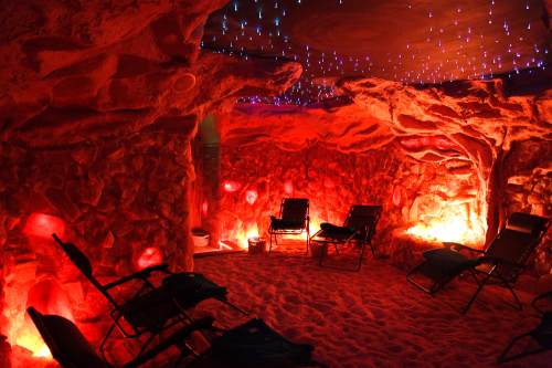 A cozy, dimly lit salt cave with red lighting, rock formations, and lounge chairs for relaxation.