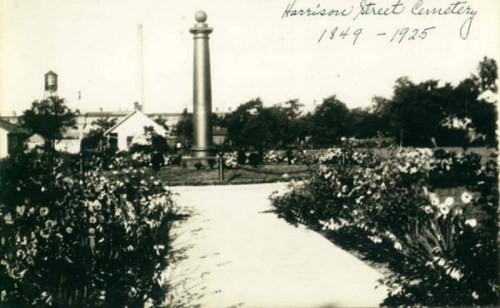 Black and white photo of Harrison Street Cemetery, featuring a monument surrounded by flowers, dated 1849-1925.