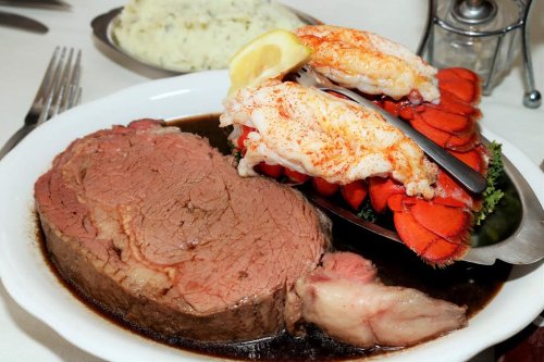 A plate featuring a large portion of prime rib topped with lobster tail and served with a side of mashed potatoes.
