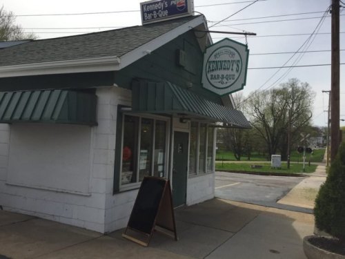 Exterior of Kennedy's Bar-B-Que, featuring a green and white building with a sign and a chalkboard outside.
