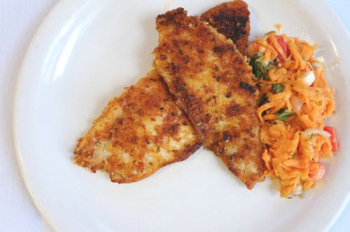 Two golden-brown fish fillets served on a white plate with a side of colorful shredded vegetable salad.