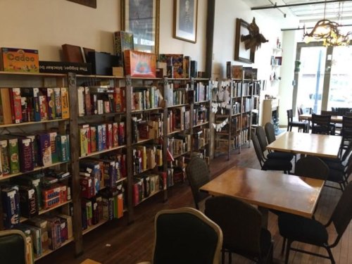 A cozy café with wooden shelves filled with board games and tables for patrons to enjoy.