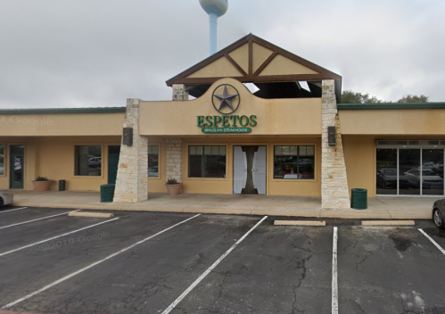 Exterior of Espetos Brazilian Steakhouse, featuring a stone and stucco facade with a star logo and parking lot.